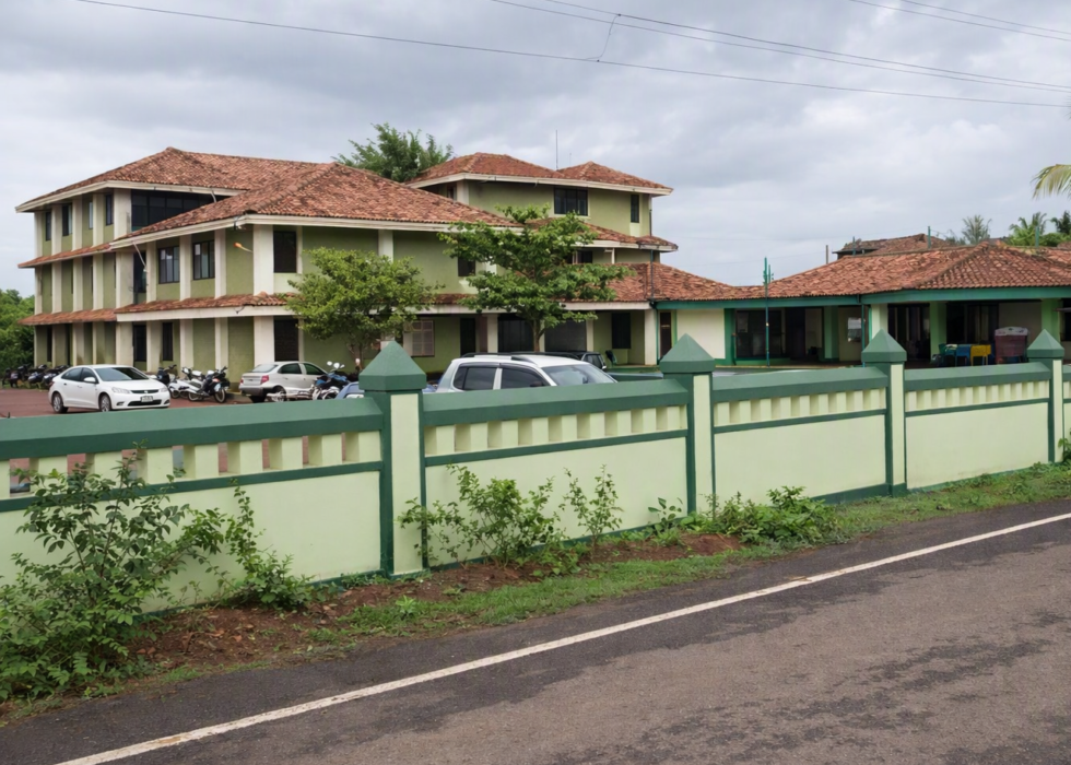 A bright, high‑definition view of the Anjuna Police Station building with green walls, terracotta roofs, and a neat boundary wall along the roadside.