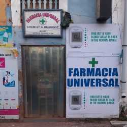The image shows the storefront of Farmacia Universal, a well-known pharmacy located on Filipe Neri Xavier Road, Fontainhas, Panaji, Goa.