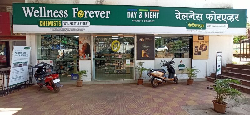 The image shows the Wellness Forever Pharmacy storefront located at Socorro Panchayat, Porvorim, Goa. The address visible on the sign right below the Hindi text explicitly lists Shop No. 23, Ground Floor of Sansha's Lajoy.